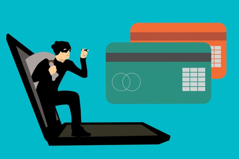 Illustrazione di un ladro informatico che esce da un laptop, con carte di credito sullo sfondo, a simboleggiare il furto di dati di pagamento