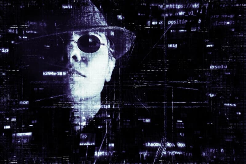 Illustrazione digitale di un volto parzialmente distorto, con cappello e occhiali scuri, sovrapposto a frammenti di codice e indirizzi web