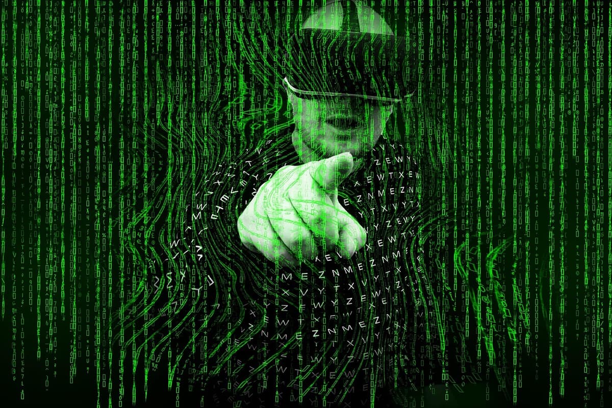 Illustrazione digitale di una figura con cappello, composta da caratteri di codice verde, che punta un dito all'interno di un motivo a spirale simile a un'impronta digitale