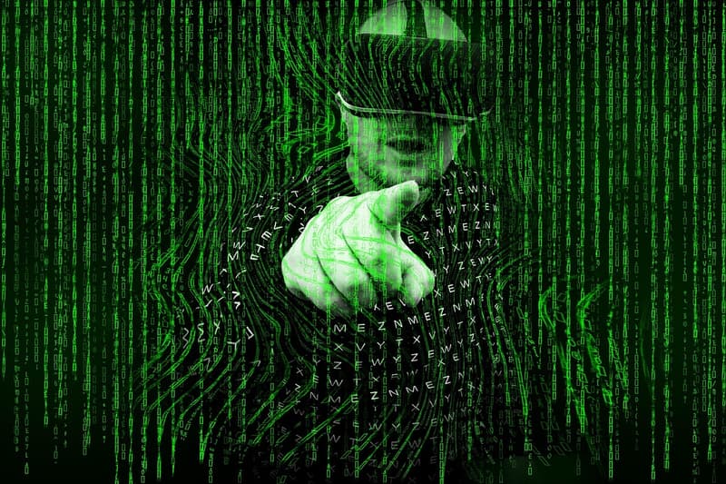 Illustrazione digitale di una figura con cappello, composta da caratteri di codice verde, che punta un dito all'interno di un motivo a spirale simile a un'impronta digitale