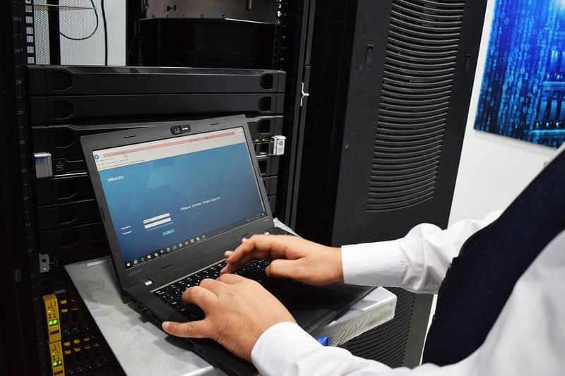 Fotografia di un tecnico al lavoro su un laptop collegato a un server rack, con la schermata di accesso VMware vCenter visibile